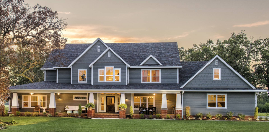 A two-story gray house with a porch and green lawn under a sunset sky.