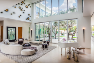 Modern living room with high ceilings, large windows, white piano, and decorative wall art.