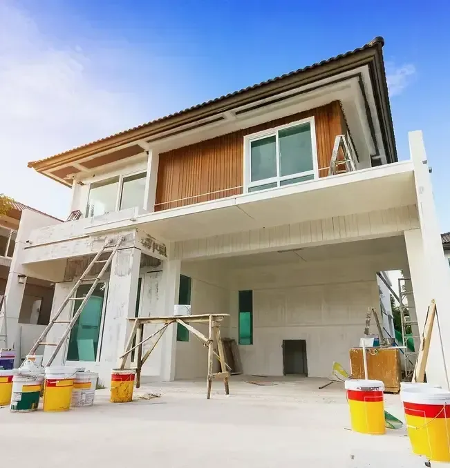 House under construction, exterior view with paint cans, ladders, and scaffolding.