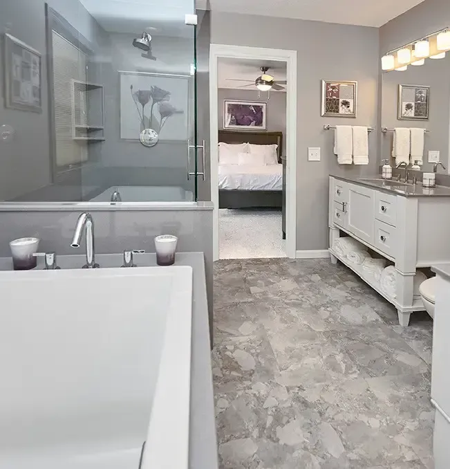 Bathroom with a white tub, walk-in shower, vanity, and open doorway to a bedroom. Gray and white color scheme.