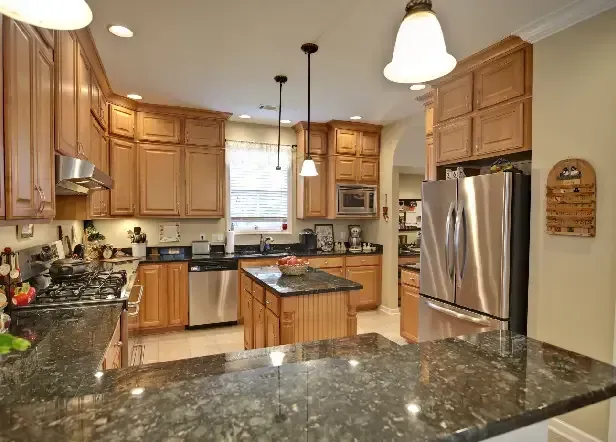 A kitchen with wooden cabinets, stainless steel appliances, and a dark granite countertop.