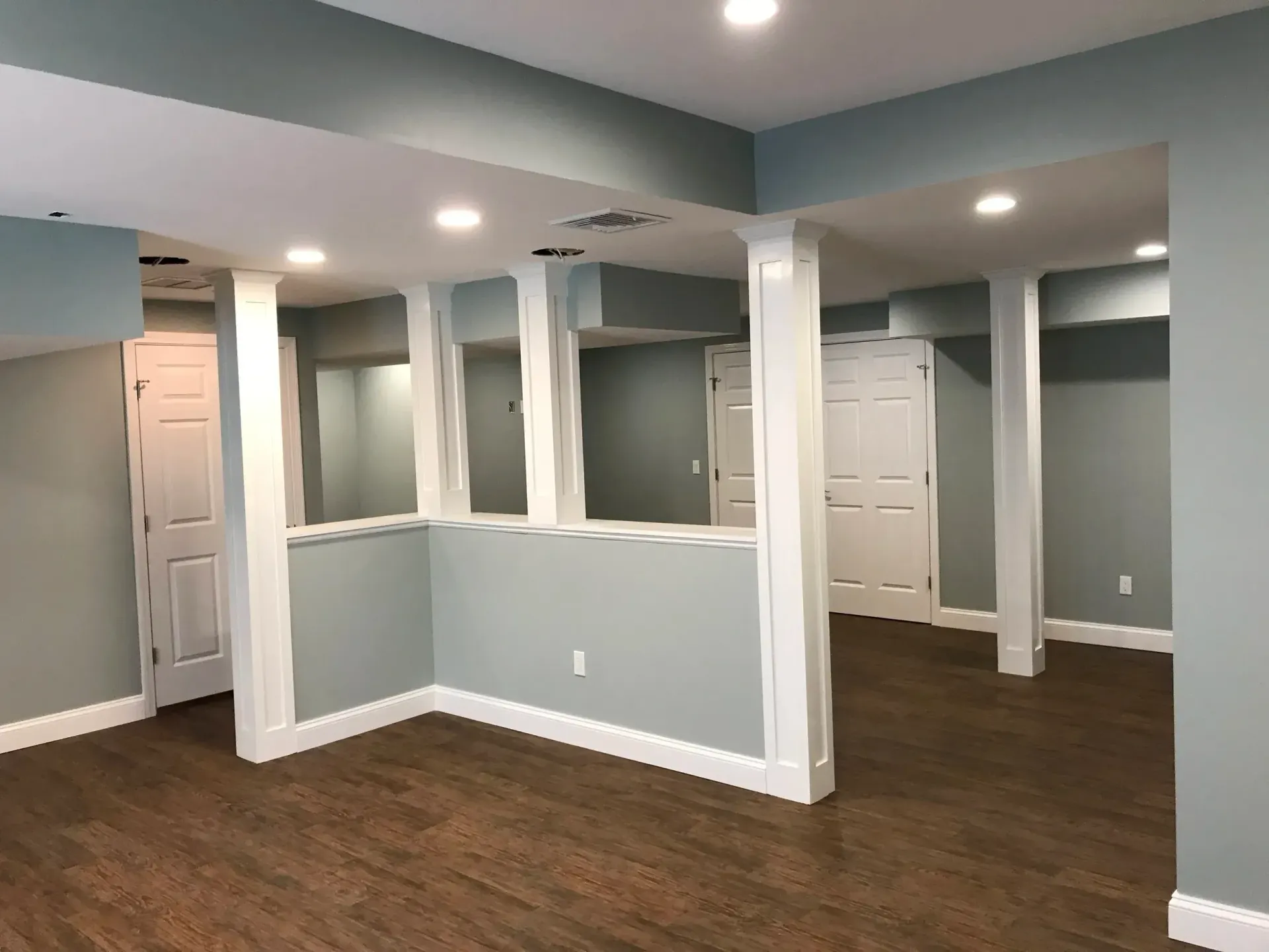Finished basement with light blue walls, white trim, recessed lighting, and brown flooring.