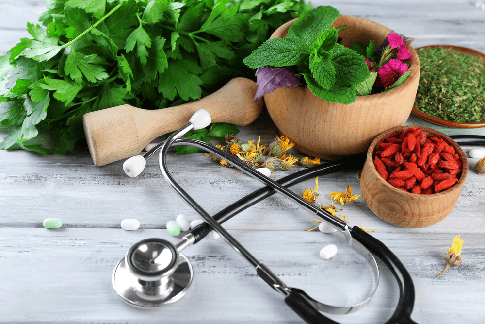 Herbs, stethoscope, and pills arranged on a wooden surface, suggesting alternative medicine.