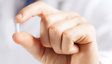Hand holding a small, white pill between thumb and forefinger.