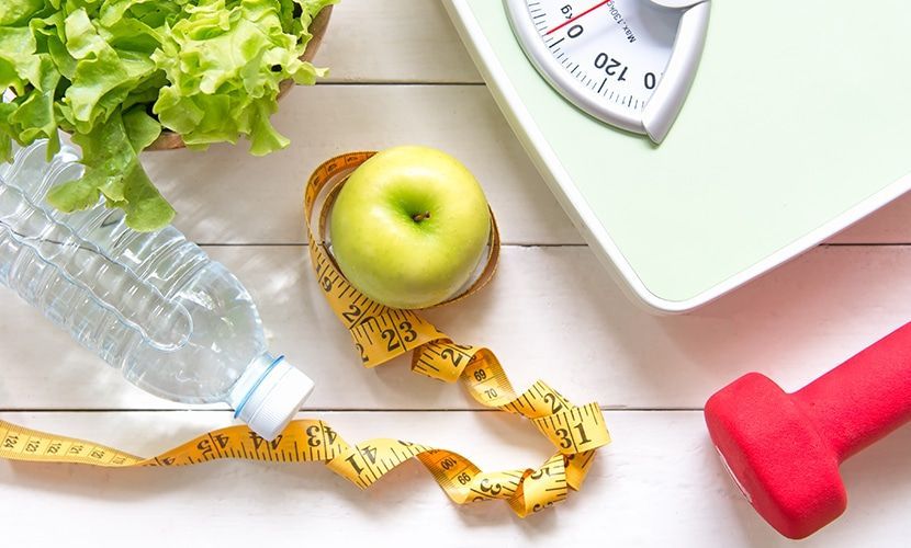 Healthy eating and exercise: green apple with tape, water bottle, lettuce, weight scale, and dumbbell.