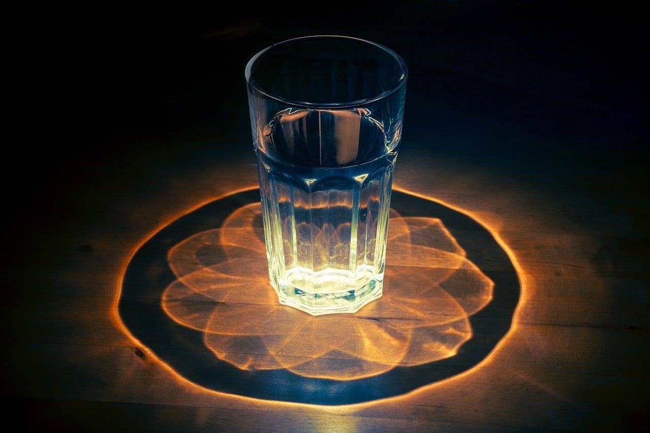 Glass of water casts a flower-shaped light pattern on a dark surface.