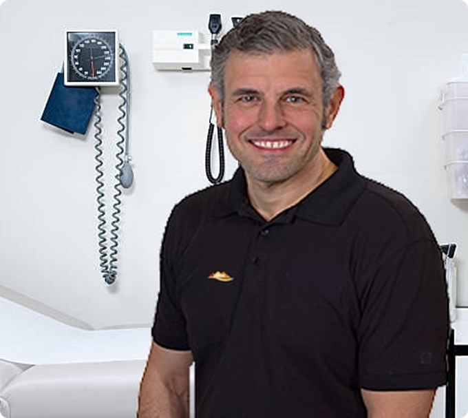Smiling doctor in a black shirt in an examination room with blood pressure equipment on the wall.