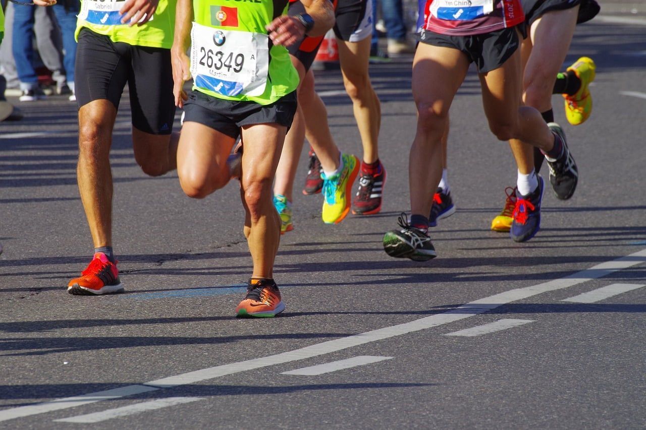 Runners in a race on a sunny day; asphalt road with white lines, colorful running shoes.