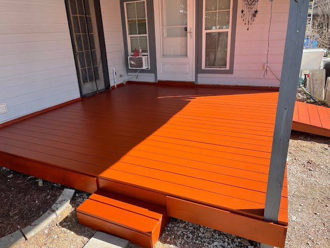 A wooden deck is painted orange in front of a white house.
