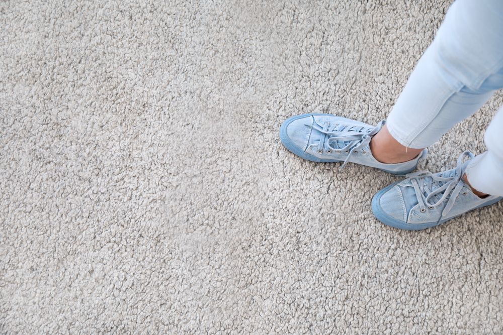 Light Blue Sneakers and Jeans Standing on a Beige Carpet Floor — Queanbeyan Carpets in Queanbeyan, NSW