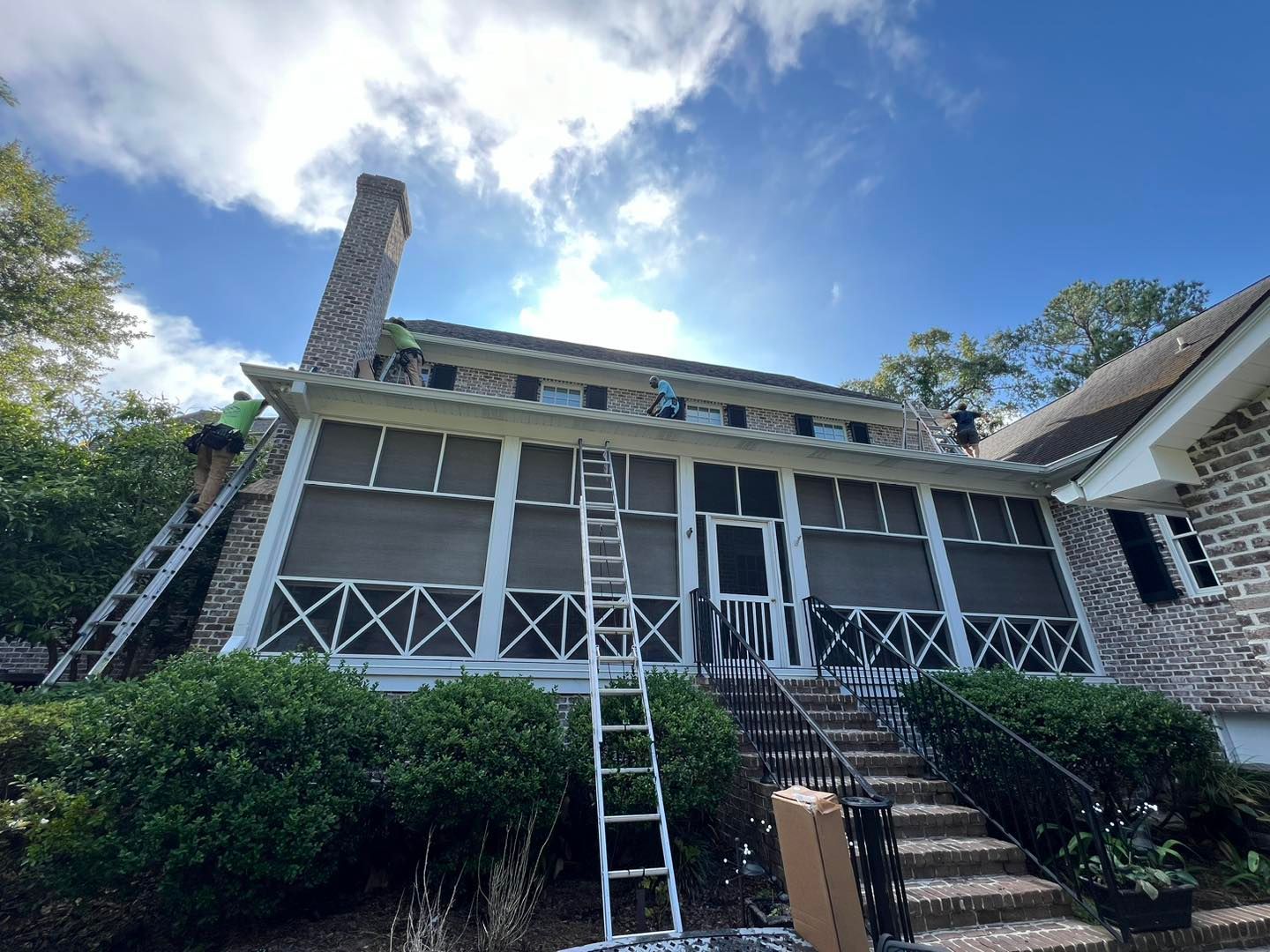 A large brick house with a screened in porch is being painted.