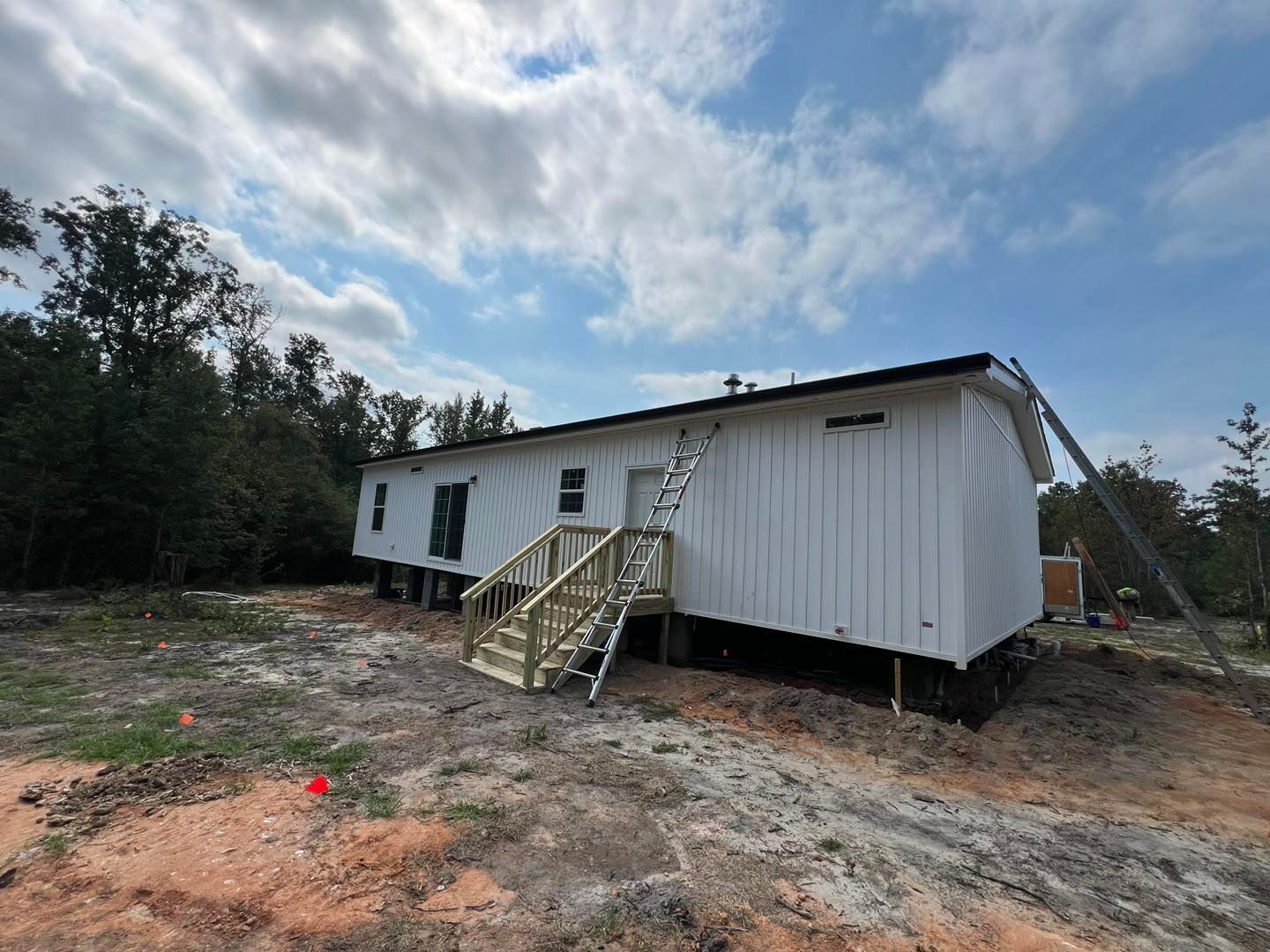 A white mobile home with a wooden deck and stairs.