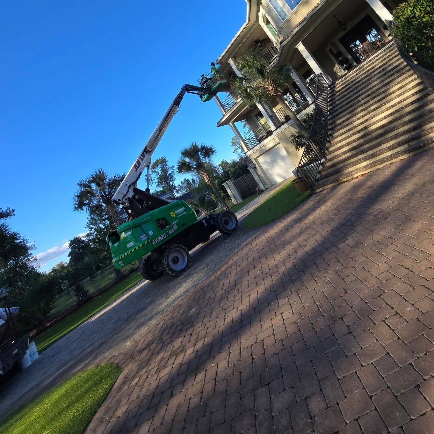 A green crane is parked in front of a large house