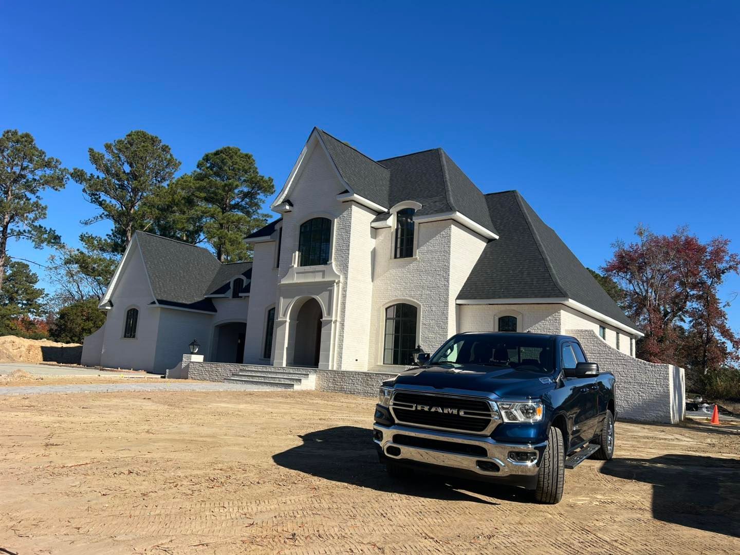 A blue ram truck is parked in front of a large white house under construction.