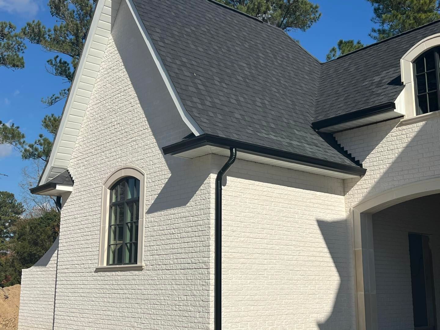 A white brick house with a black gutter and a black roof.