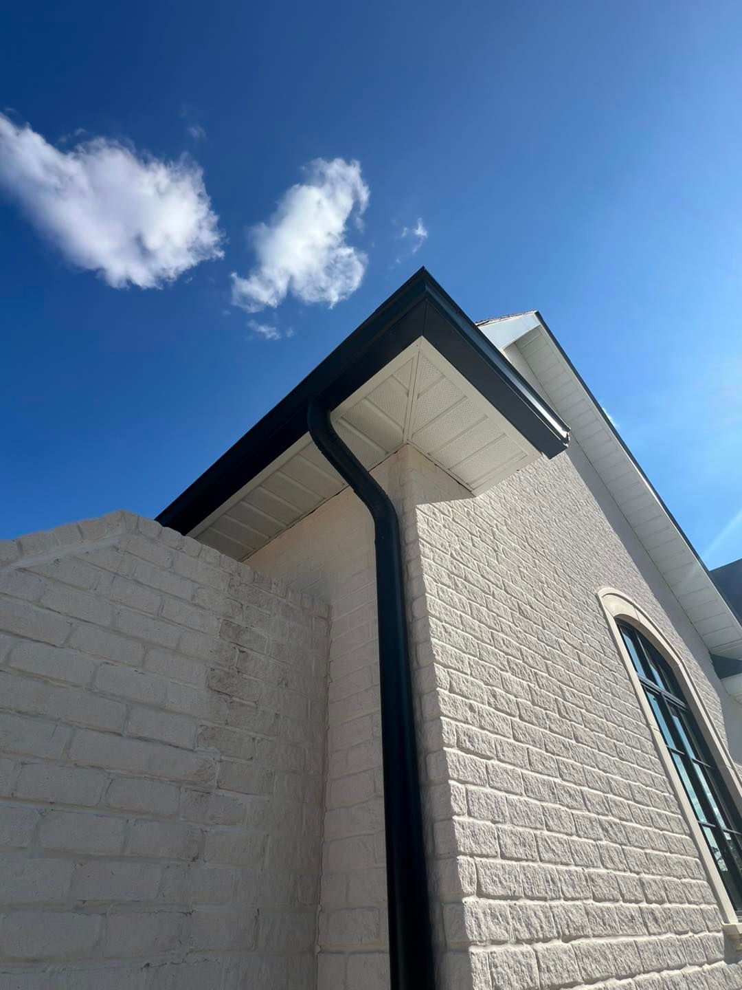 A white brick building with a black gutter and a window