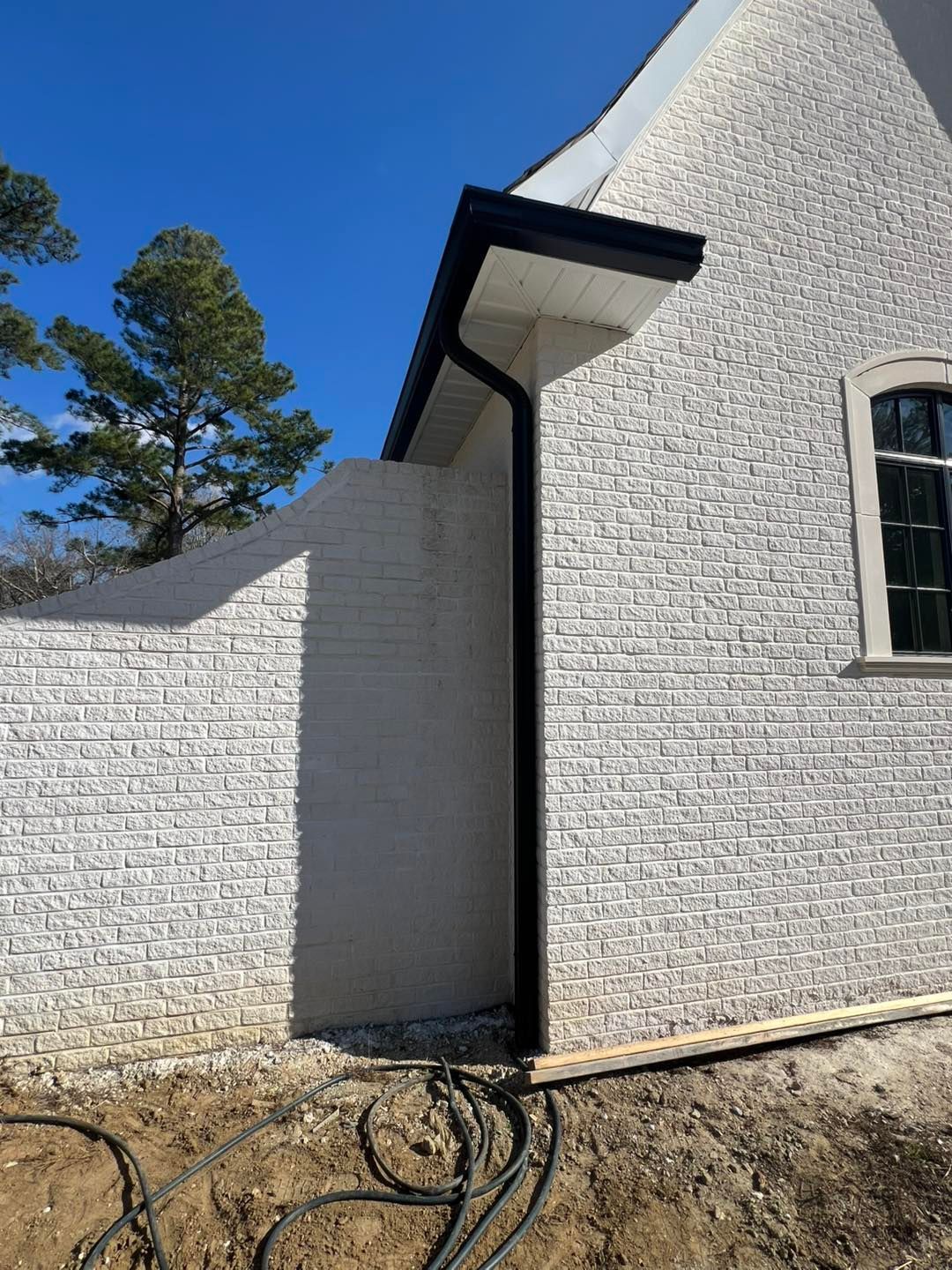 A white brick house with a black gutter on the side of it.