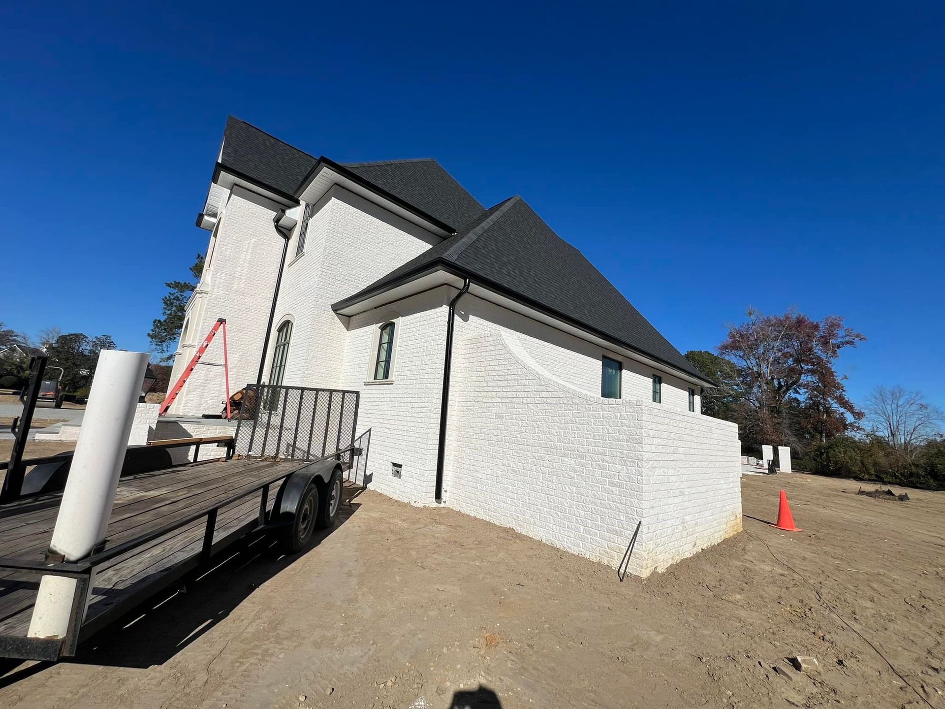 A white house is being built with a trailer parked in front of it.
