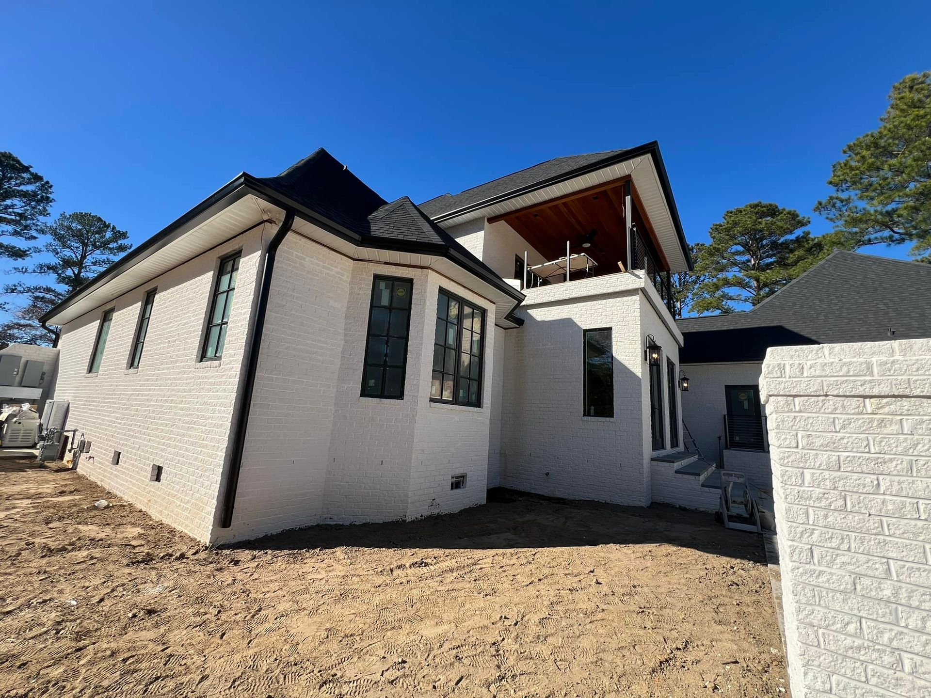 A white house with a black roof is sitting on top of a dirt field.