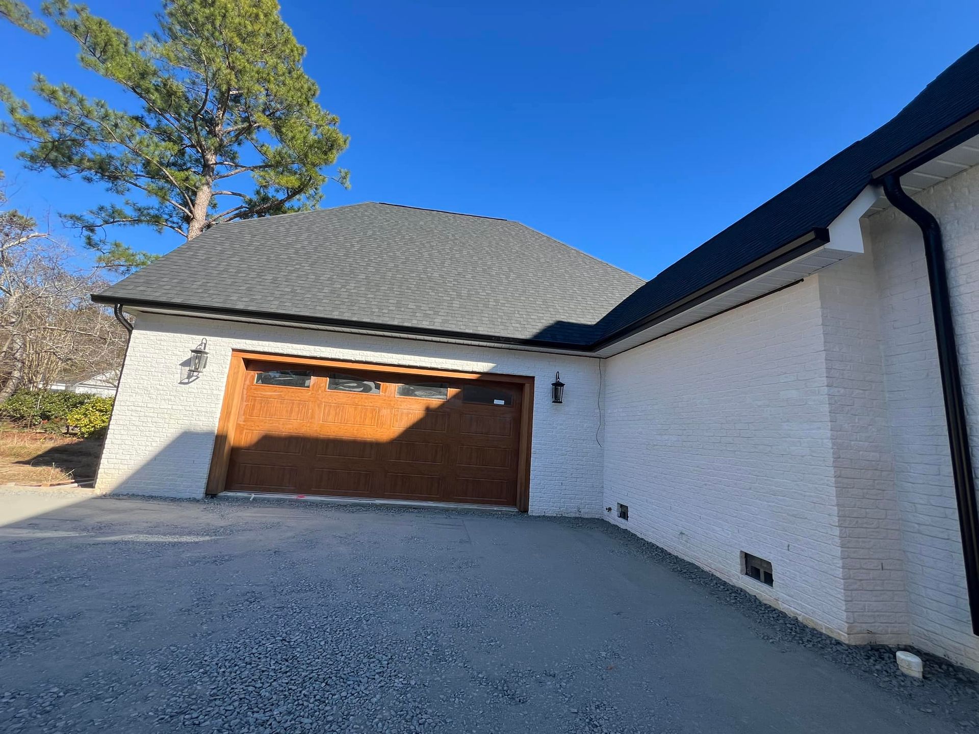 A white house with a wooden garage door and a black gutter.