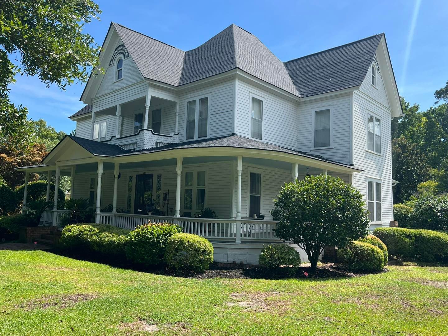 A large white house with a large porch on a sunny day.