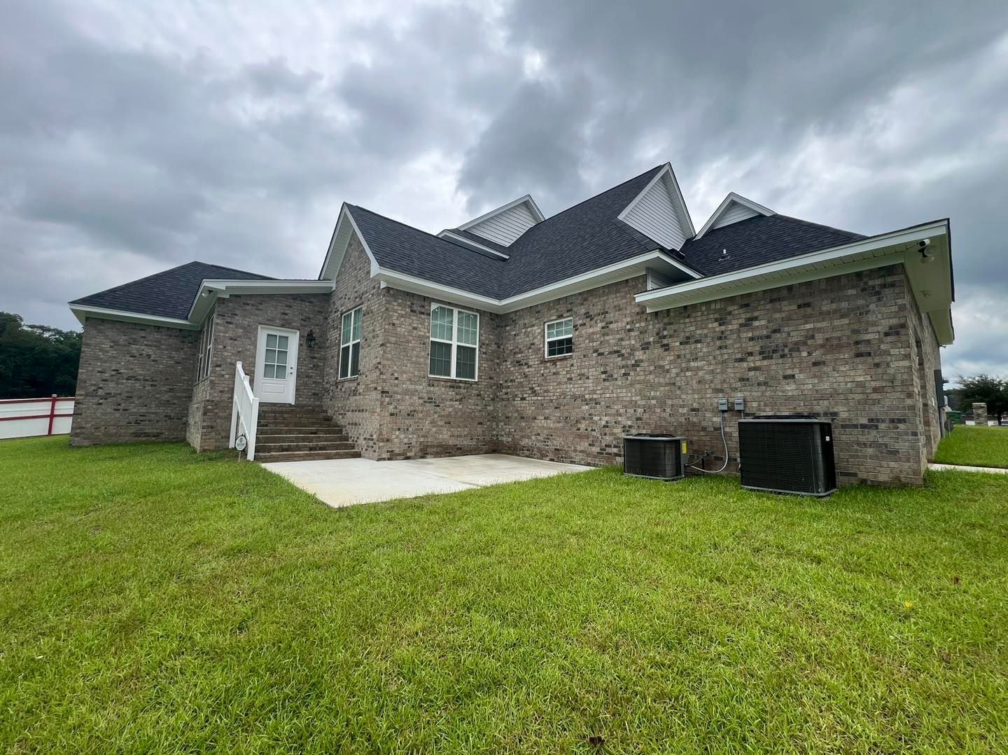 A large brick house with a black roof is sitting on top of a lush green lawn.