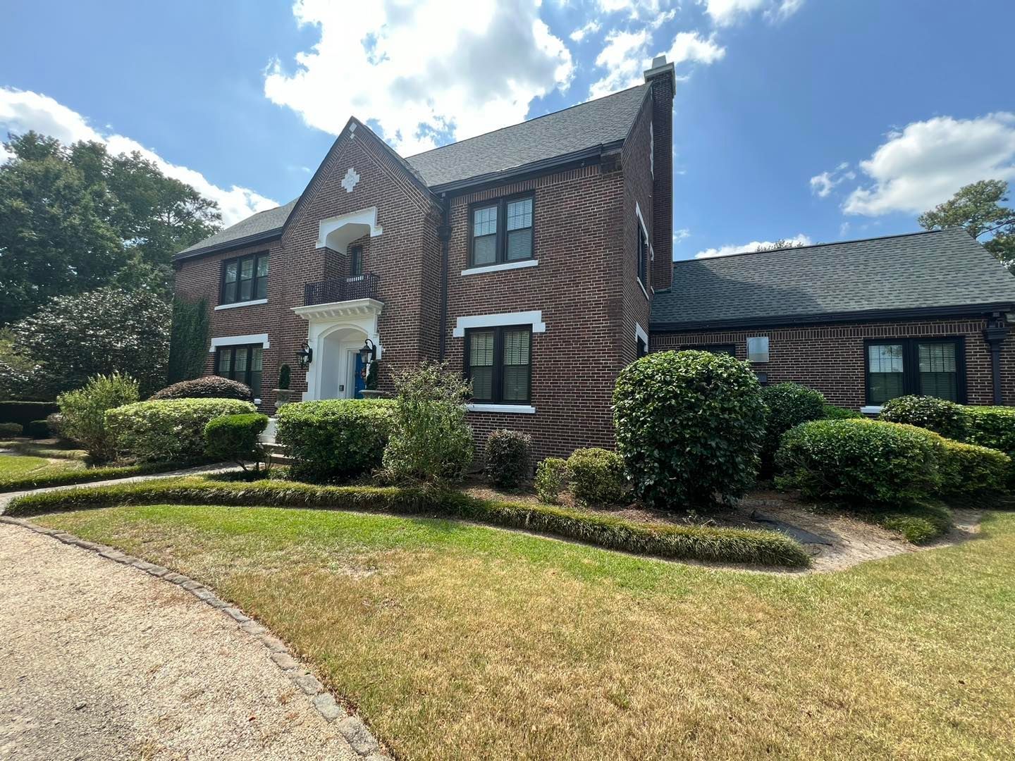 A large brick house with a lot of windows and bushes in front of it.