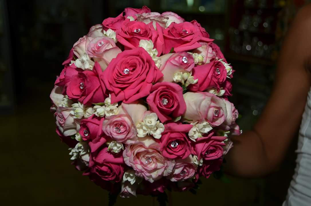 Bouquet di rose rosa e rosa chiaro con piccoli fiori bianchi, tenuto in mano da una persona che indossa un top bianco.