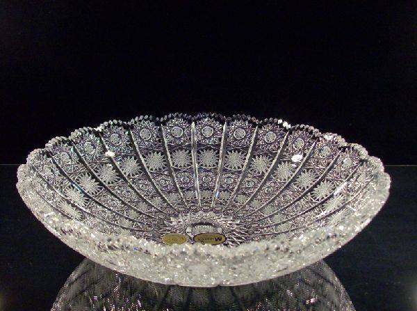 Ciotola di cristallo tagliato con intricati motivi geometrici, che riflette la luce su una superficie scura.