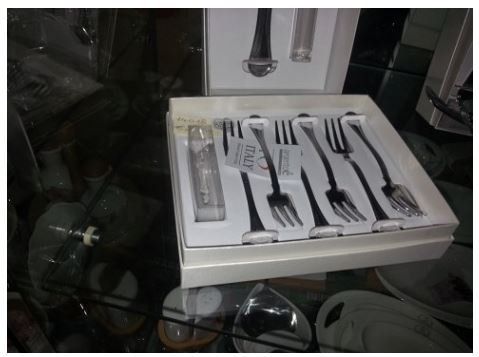 Un set di forchette nere in una scatola bianca, esposto in un negozio. L'etichetta riporta la scritta 