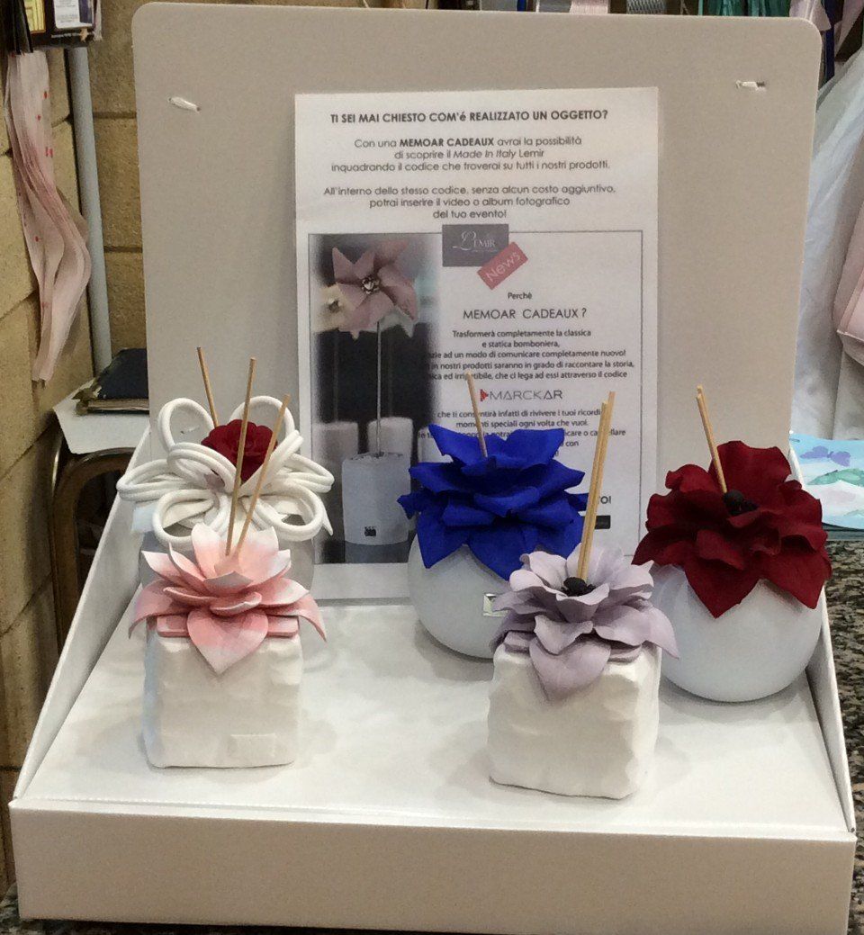 Esposizione di creazioni floreali in feltro: fiori rosa, blu, rossi e viola su blocchi e sfere bianchi.