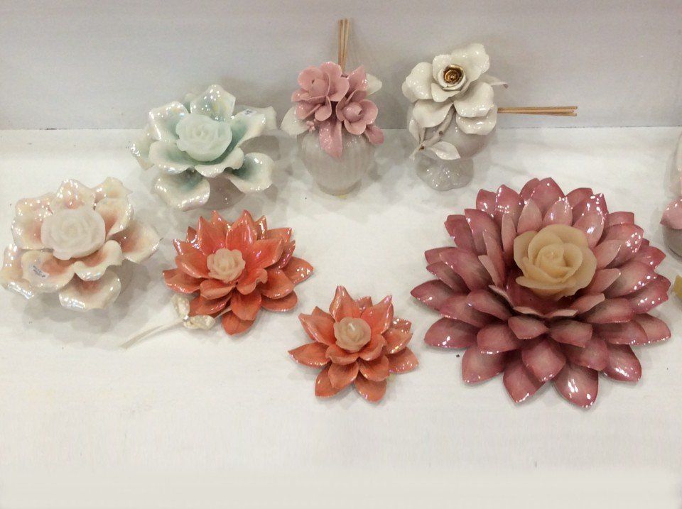 Primo piano di diversi fiori in ceramica, tra cui fiori rosa, arancioni e bianchi, su una mensola bianca.