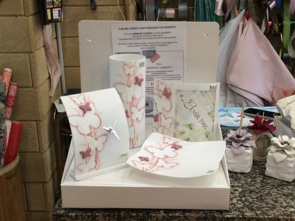 Esposizione di prodotti di carta a tema farfalla: porta fazzoletti, biglietti, piatto; bianco con dettagli rosa; ambientazione di vendita al dettaglio.