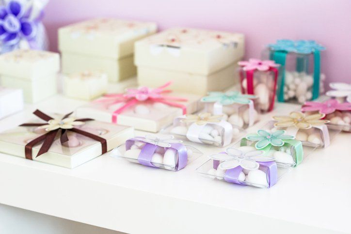 Scatole regalo assortite con nastri pastello e fiori su uno scaffale bianco.