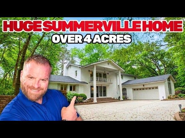 A man in a blue shirt pointing at a white house with a large garage, surrounded by trees, text reading 