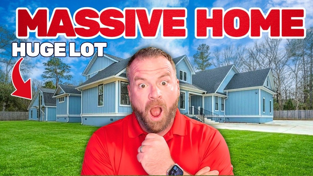 A man in a red shirt with a surprised expression stands in front of a blue farmhouse on a large, grassy lot.