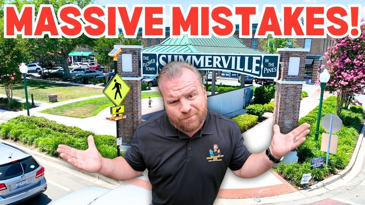 Man in black polo with arms outstretched in front of Summerville sign, cars and landscaping.