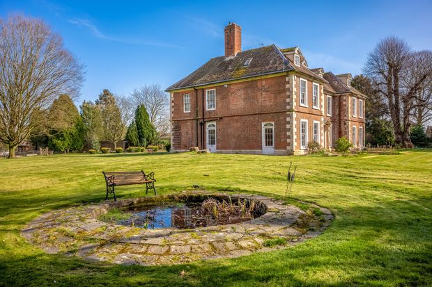 A large brick house with a pond in front of it.