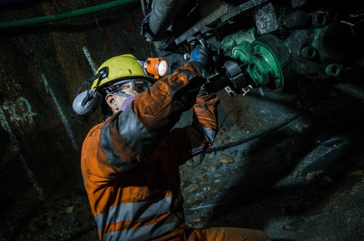 Worker in Safety Gear, Underground, Repairing Machinery with Tools. Dark Setting with Orange Overalls — Joy Hire Compressor Hire & Maintenance in Paget, QLD