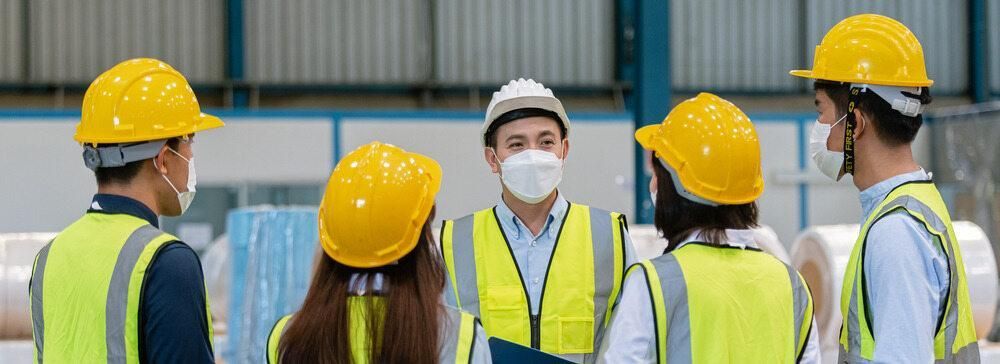 Five Workers in Safety Vests and Hard Hats Meet in A Warehouse. All Are Wearing Masks — Joy Hire Compressor Hire & Maintenance in Paget, QLD