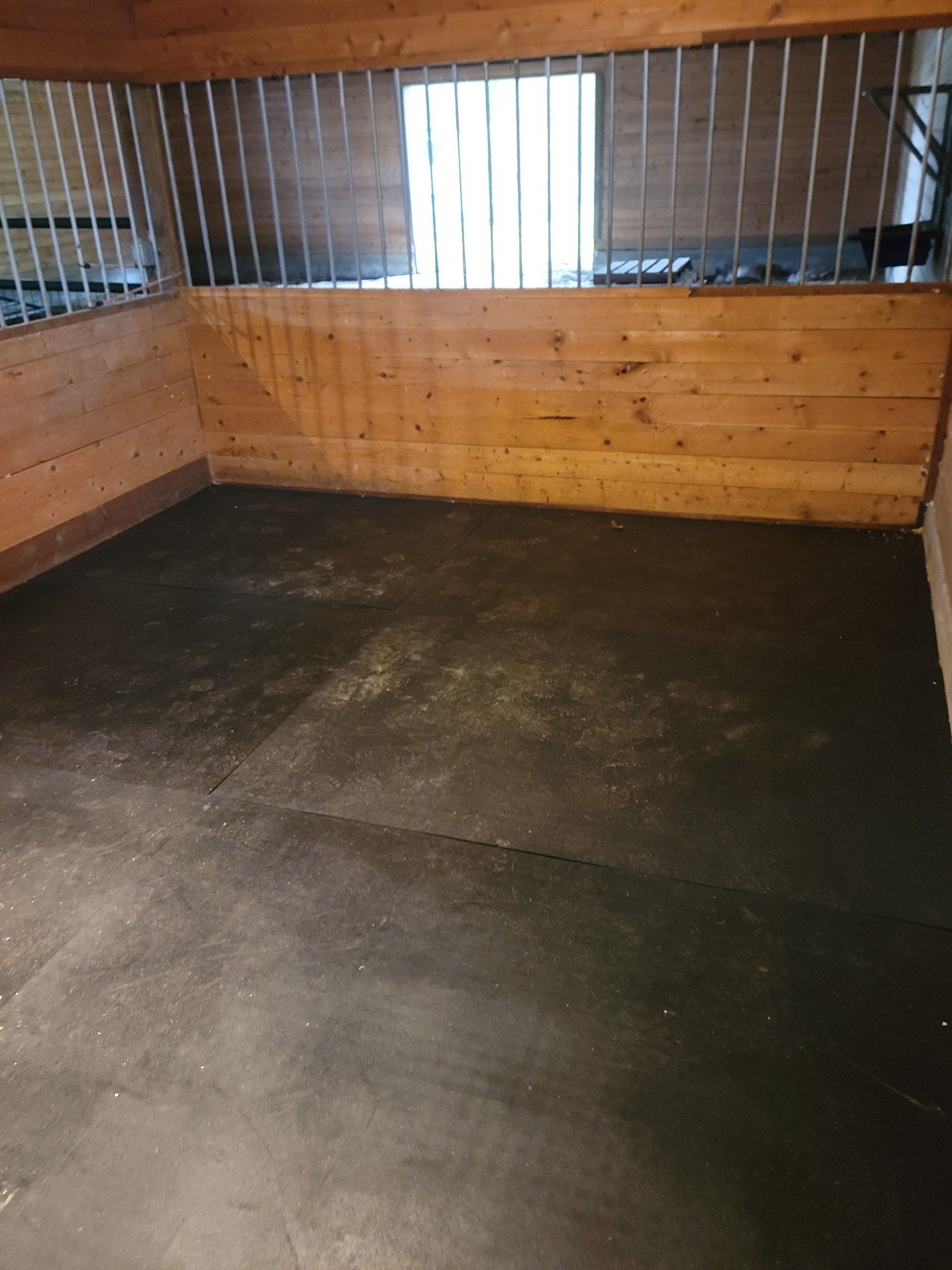 A horse stable with a black mat on the floor and a wooden wall.