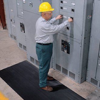 A man wearing a hard hat is working on an electrical panel.