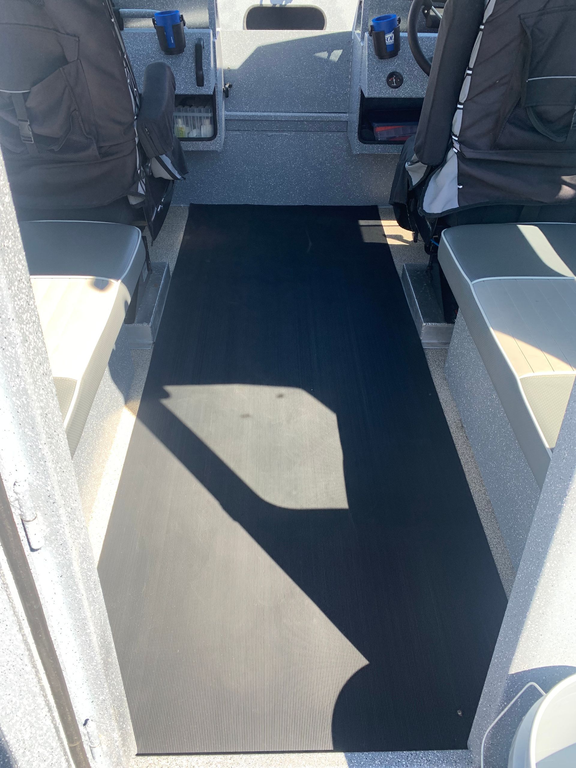 The inside of a boat with a black mat on the floor.