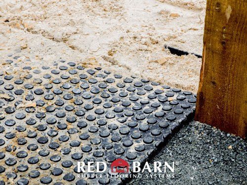 A black rubber mat is sitting on top of a sandy surface next to a wooden post.