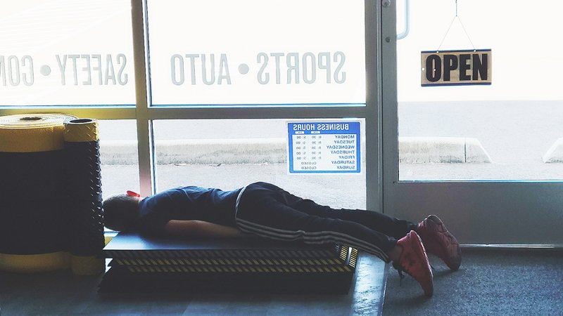 A person is laying on a bench in front of an open door.