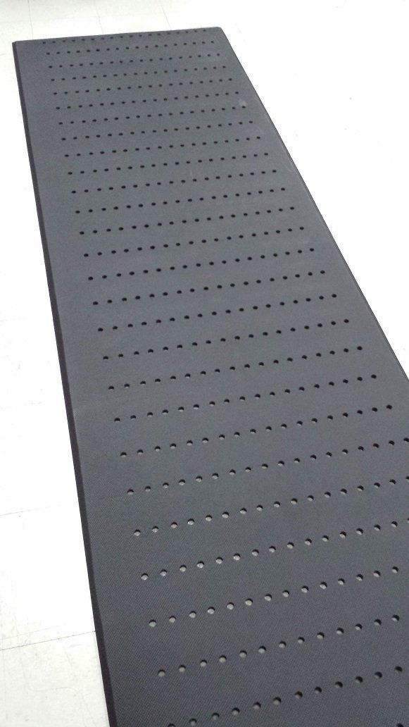 A black mat with holes in it is sitting on a white surface.