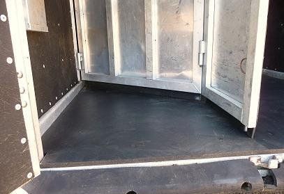 The inside of a trailer with the doors open and a black floor.