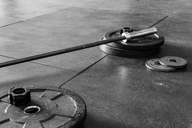 A black and white photo of a barbell and weights on the floor.