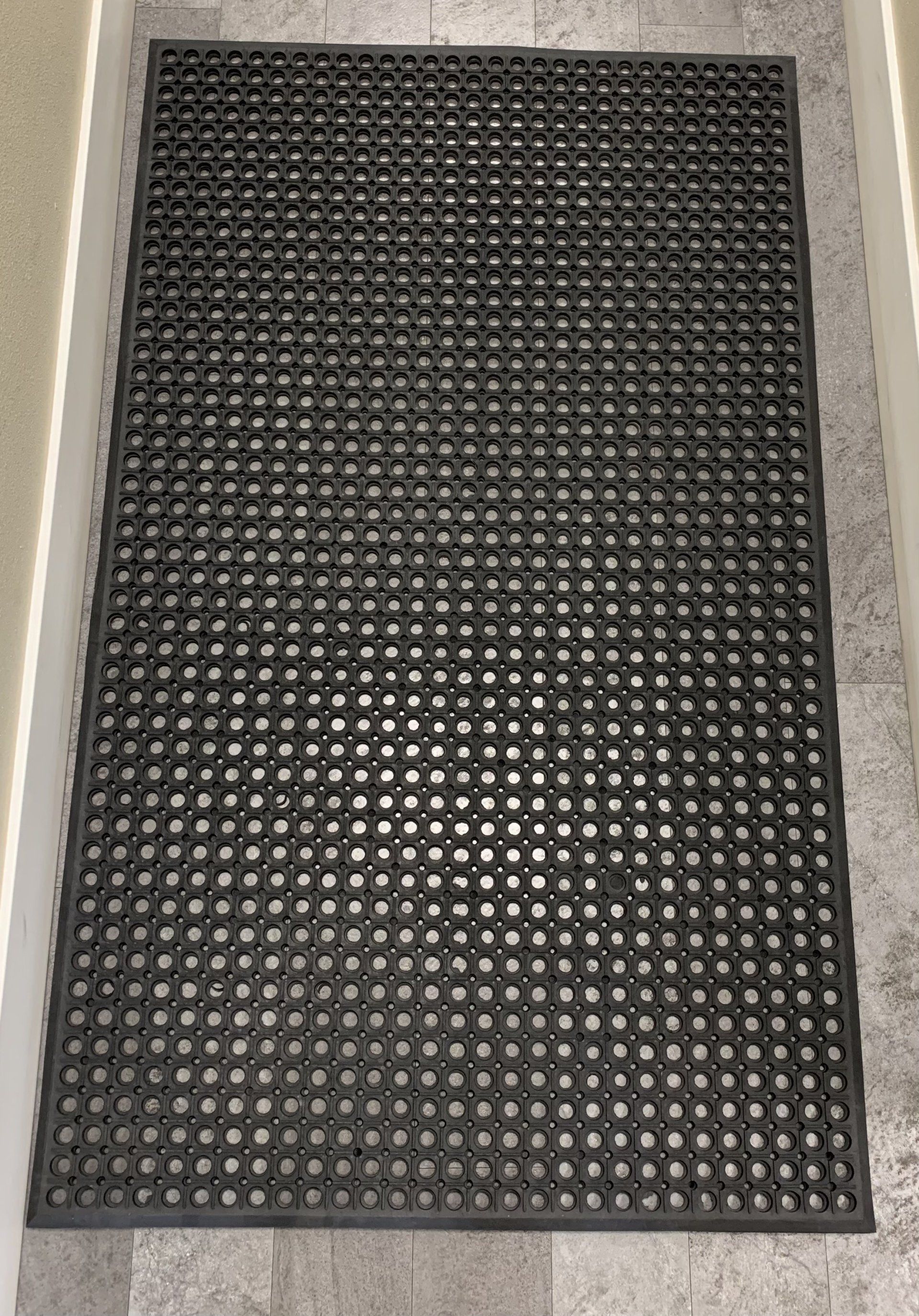 A black mat with holes in it is on a tiled floor