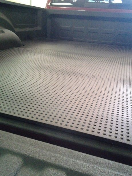 The back of a truck with a rubber mat in the bed